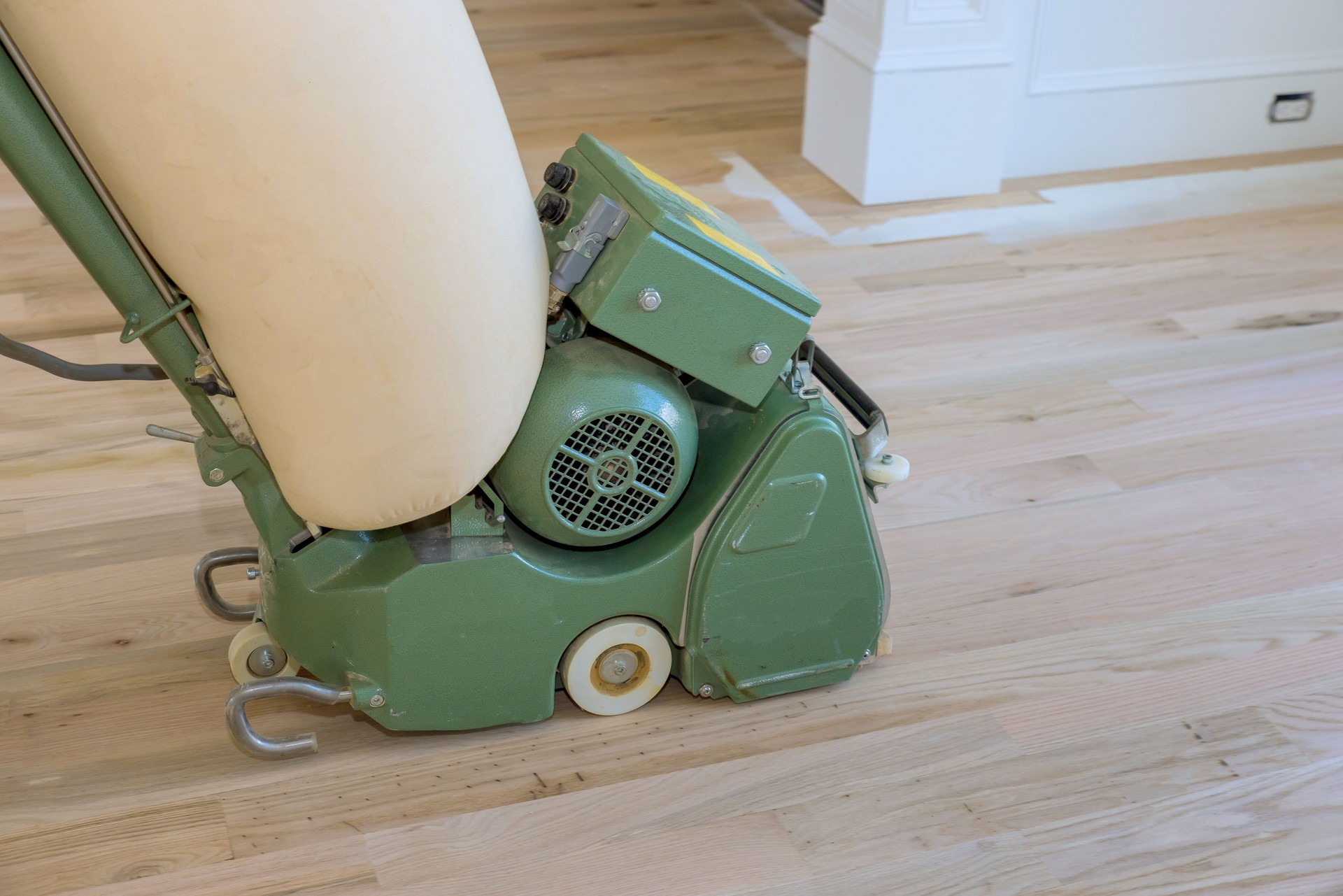 Wooden parquet floor being ground by carpenter using floor sander in a newly constructed home
